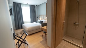 Habitación de hotel moderna con cama, escritorio, ducha y vistas al exterior.