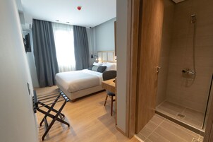 Moderni hotellihuone, jossa on sänky, työpöytä, suihku ja näkymä ulos.