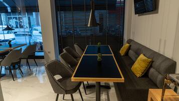 Un intérieur moderne avec un coin repas comprenant une table et des chaises noires, un canapé avec des coussins jaunes et une vue dégagée grâce à de grandes fenêtres.