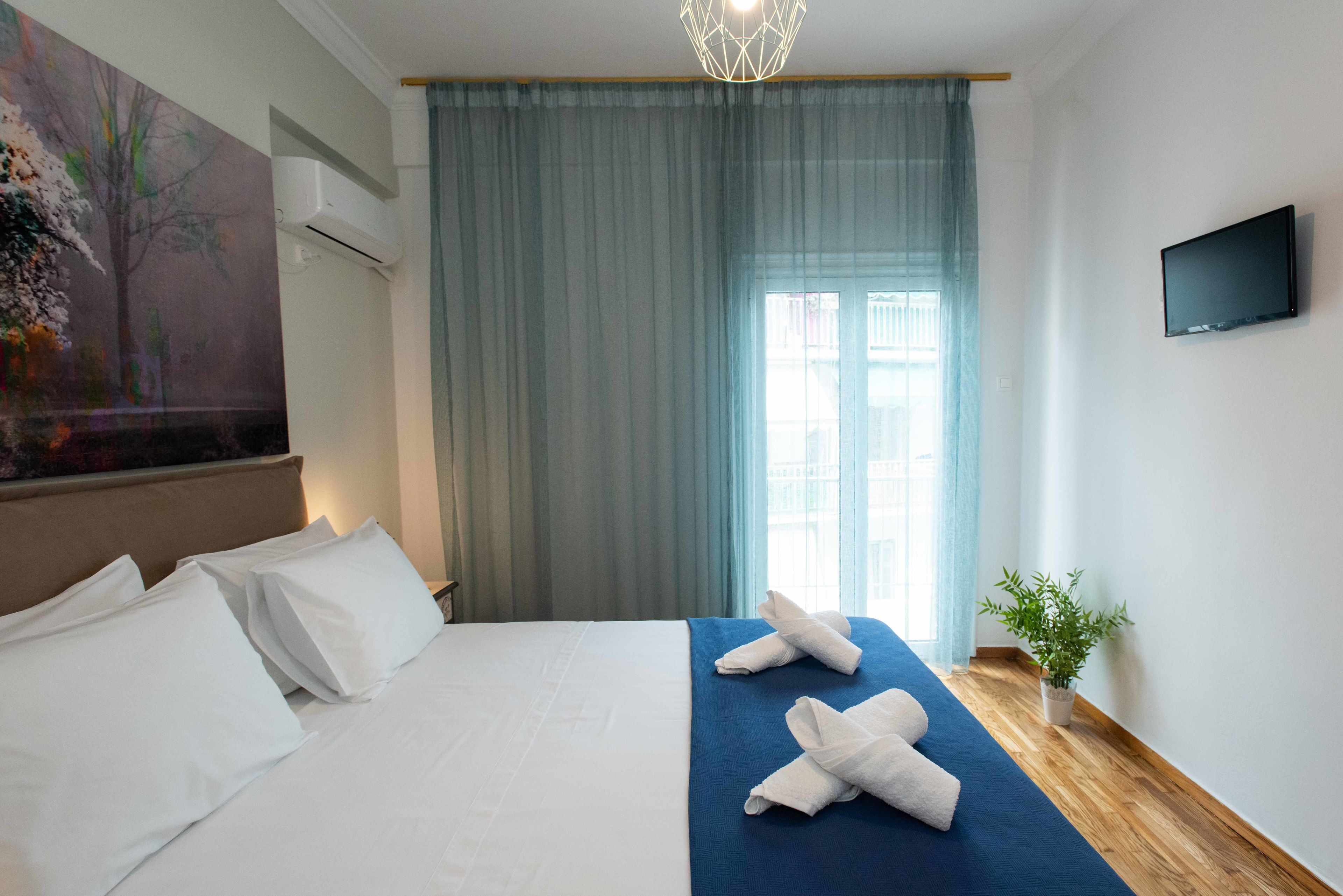 Ett hotellrum med en säng, en tv, ett fönster med gardiner och en tavla på väggen.