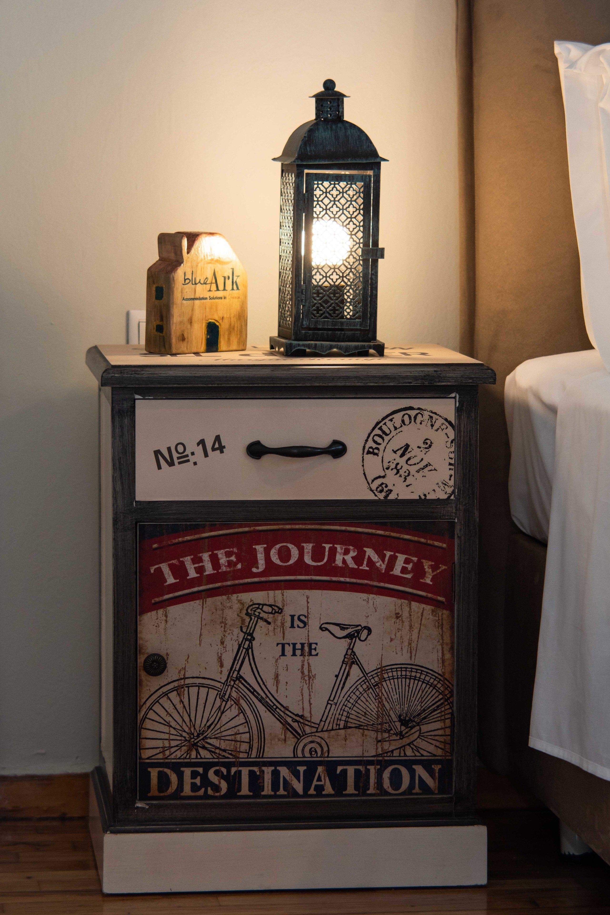 Een nachtkastje in vintage stijl met een fietsontwerp, een klein houten huismodel en een lichtgevende lantaarn.