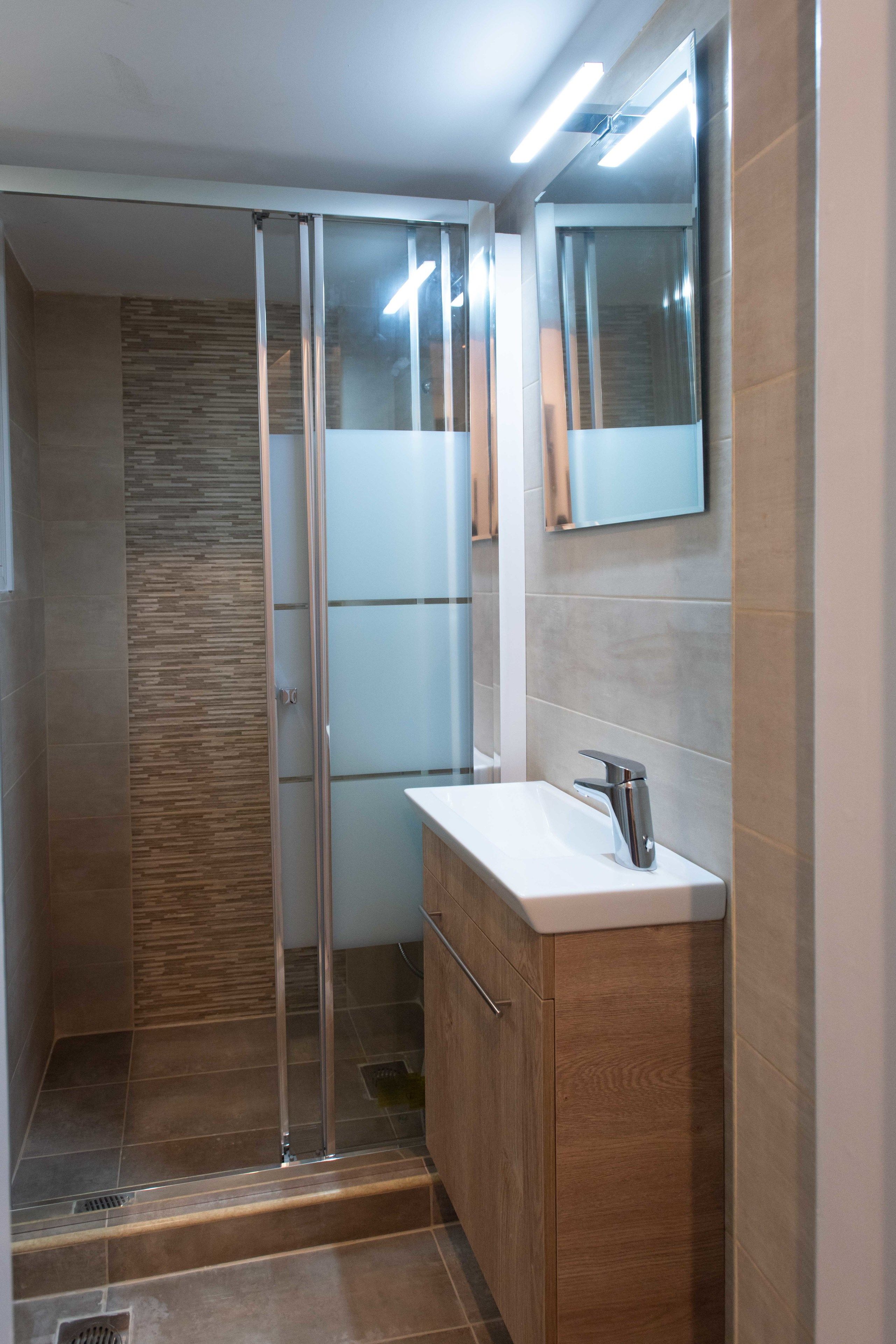 Een moderne badkamer met een douchecabine van glas, een houten wastafelmeubel en een grote spiegel.