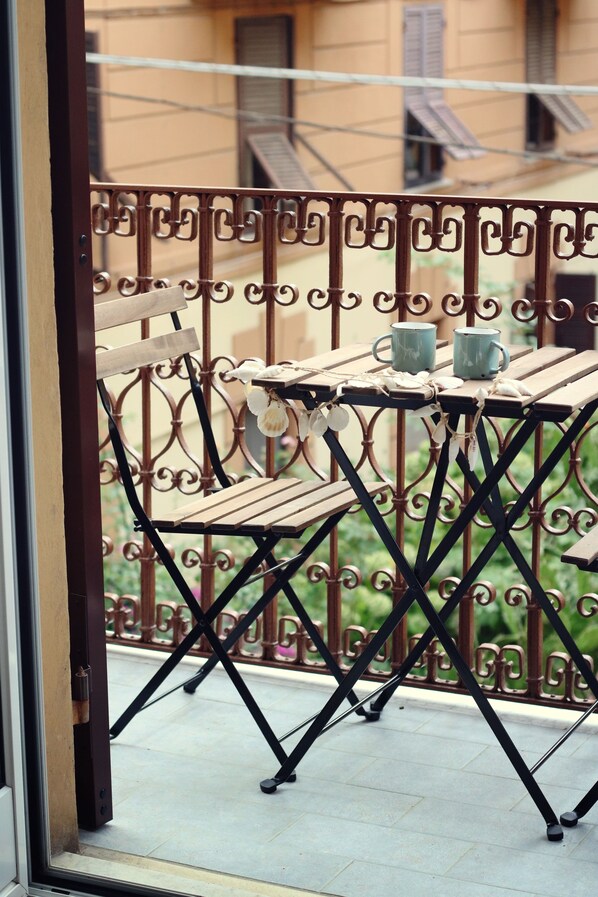 A balcony with a wrought iron railing, a wooden table with two blue mugs, and a chair.