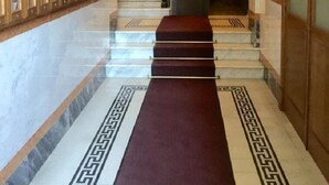 Un couloir en marbre, avec un tapis rouge menant à un escalier.