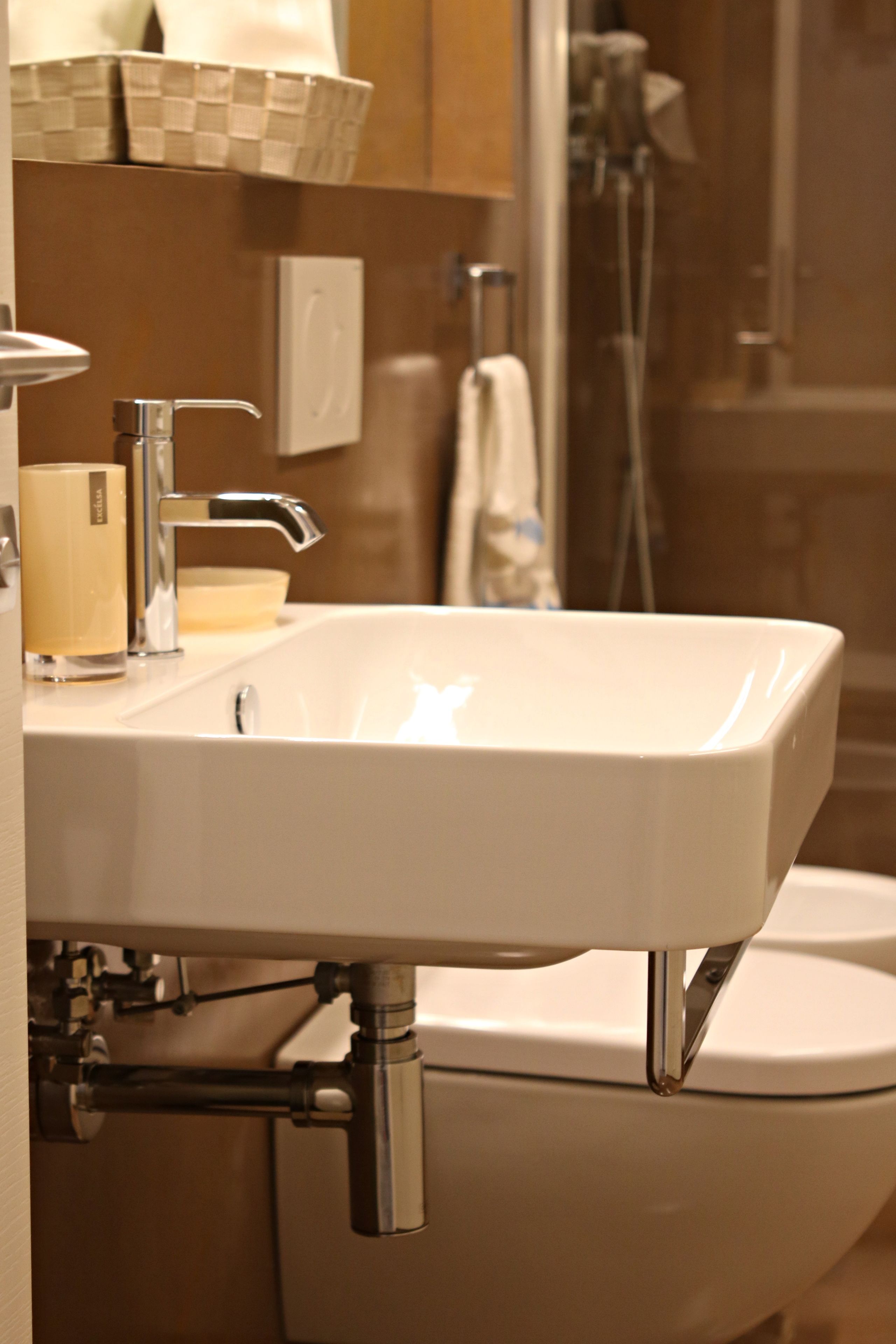 A bathroom with a white sink, chrome faucet, and a toilet. There is a towel rack and a soap dispenser on the wall.