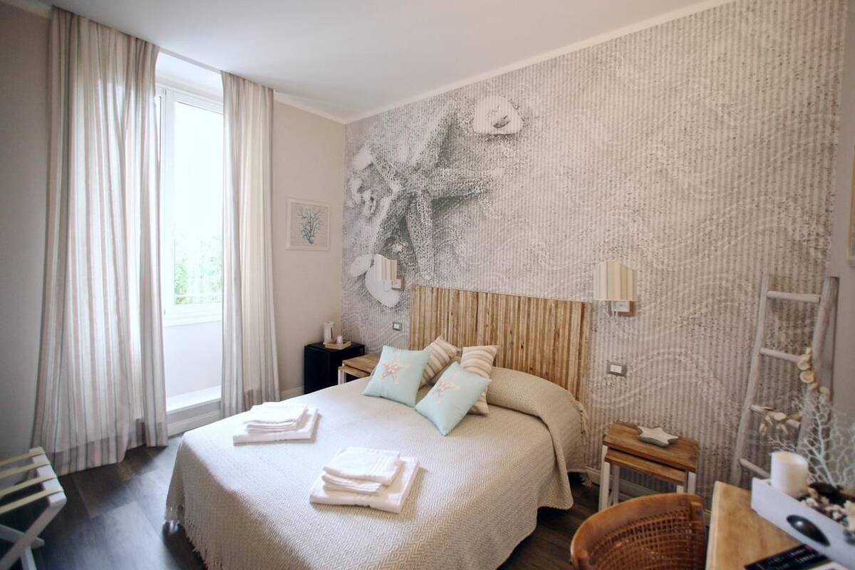 Een slaapkamer met een bed, nachtkastje, stoel en raam met gordijnen.