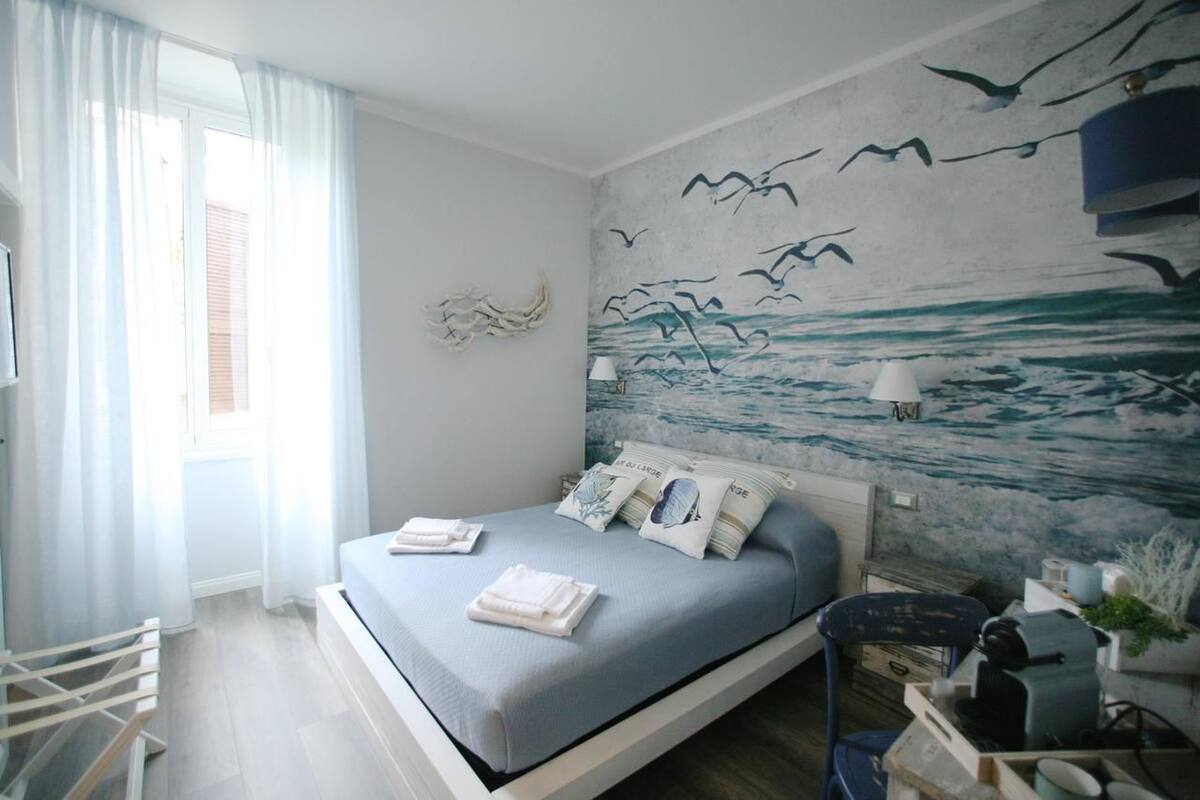 Een slaapkamer met een bed, een raam met gordijnen, een vogelwanddecoratie en een lamp.