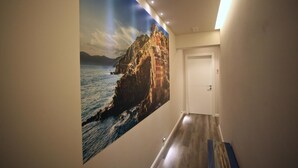Un couloir orné d’une grande fresque représentant un paysage côtier, doté d’un plancher en bois et d’une porte blanche.