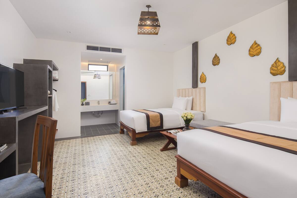 Une chambre d’hôtel avec deux lits, une télévision, un bureau et une salle de bain visible à travers une porte ouverte.