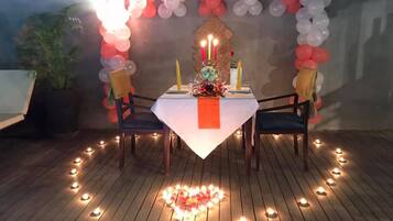 Uma área de refeições ao ar livre com uma mesa posta para dois, rodeada por balões e velas.