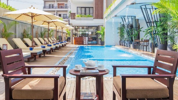 Un espace aménagé au bord de la piscine, avec des chaises longues et des parasols, une piscine, ainsi qu’un bar avec des sièges.