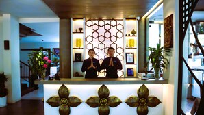 Un comptoir d’accueil agrémenté d’un panneau décoratif aux motifs géométriques, d’un menu encadré et d’une plante en pot.