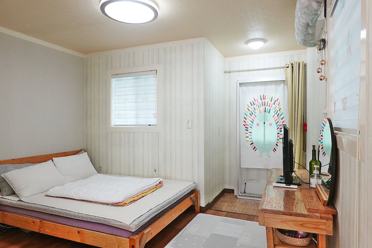 A bedroom with a bed, a small table with a bottle, and a decorative item on the wall.