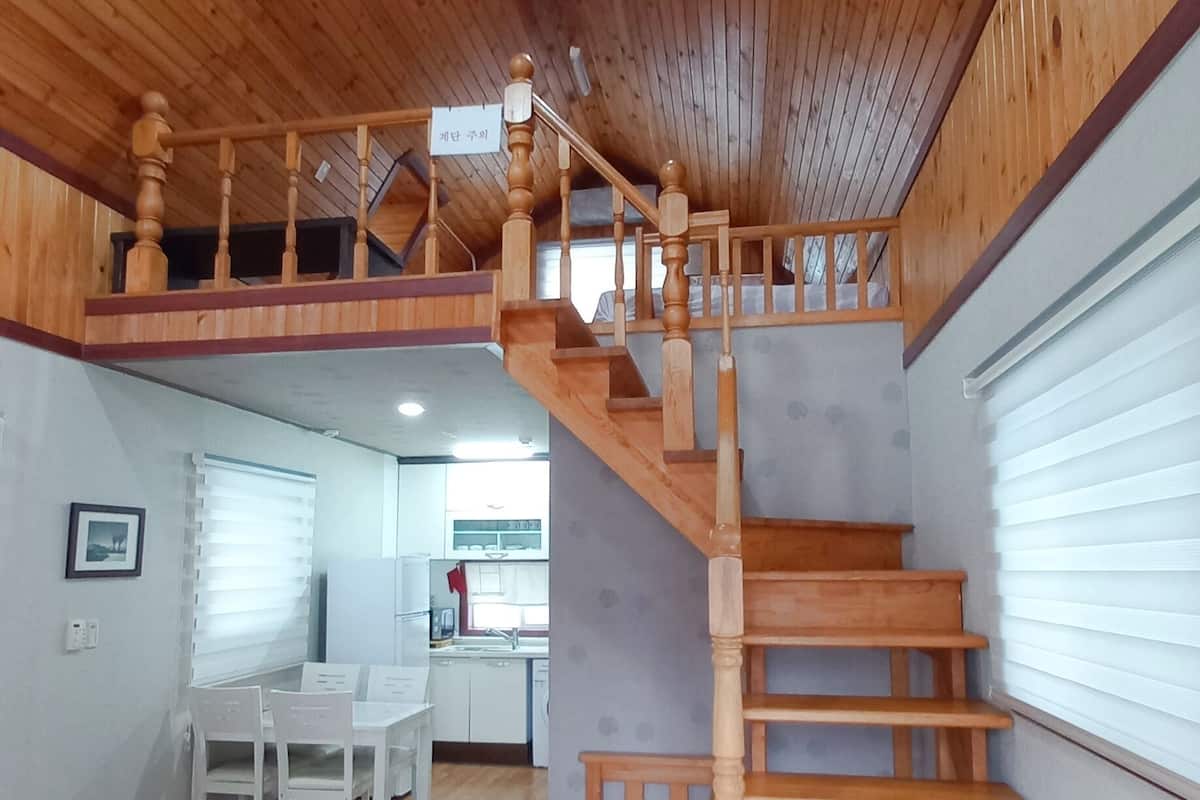 A wooden staircase in a room with a kitchen in the background.