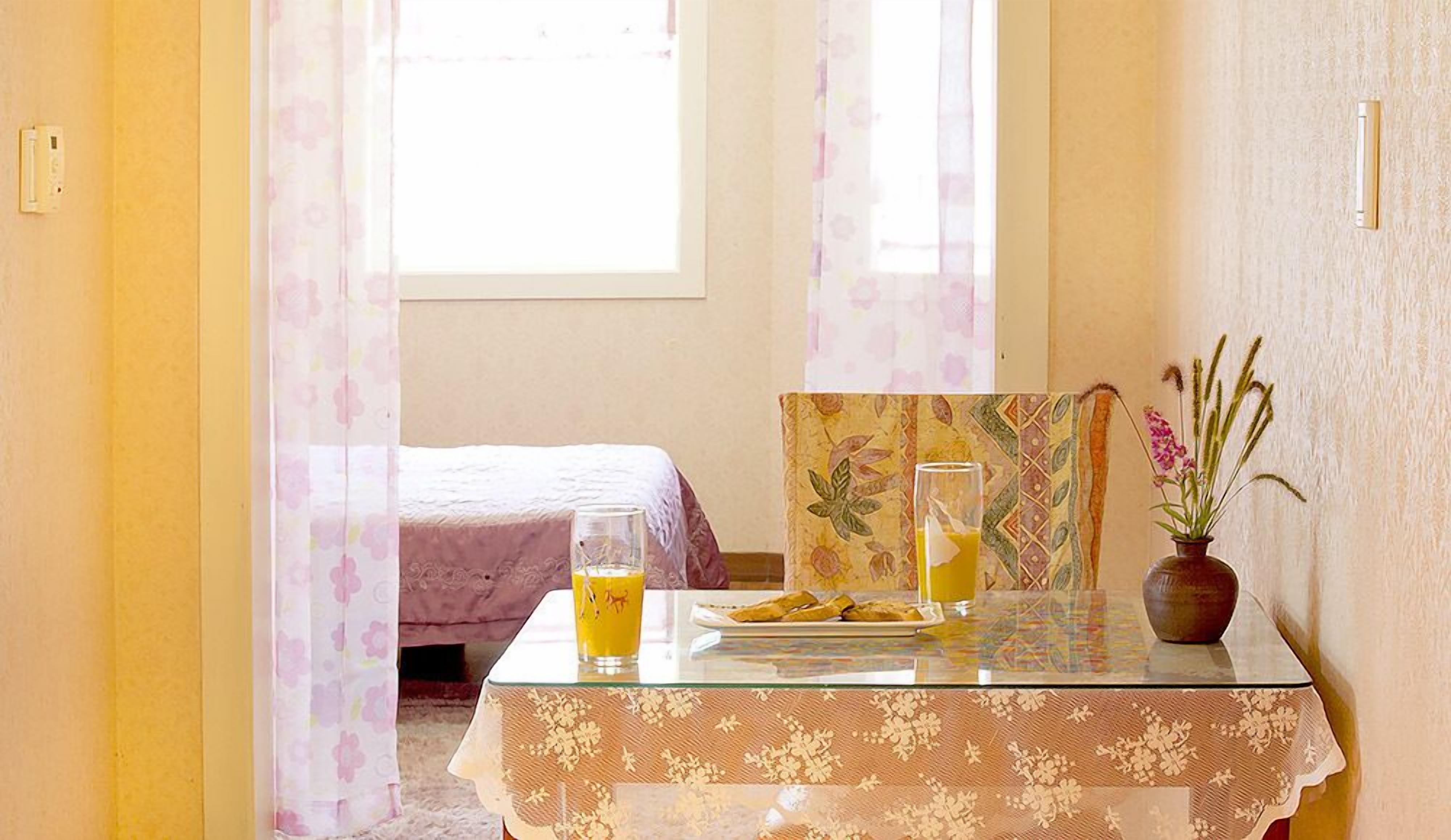 Una habitación de hotel con cama, una mesa con cosas para el desayuno y una ventana con cortinas.