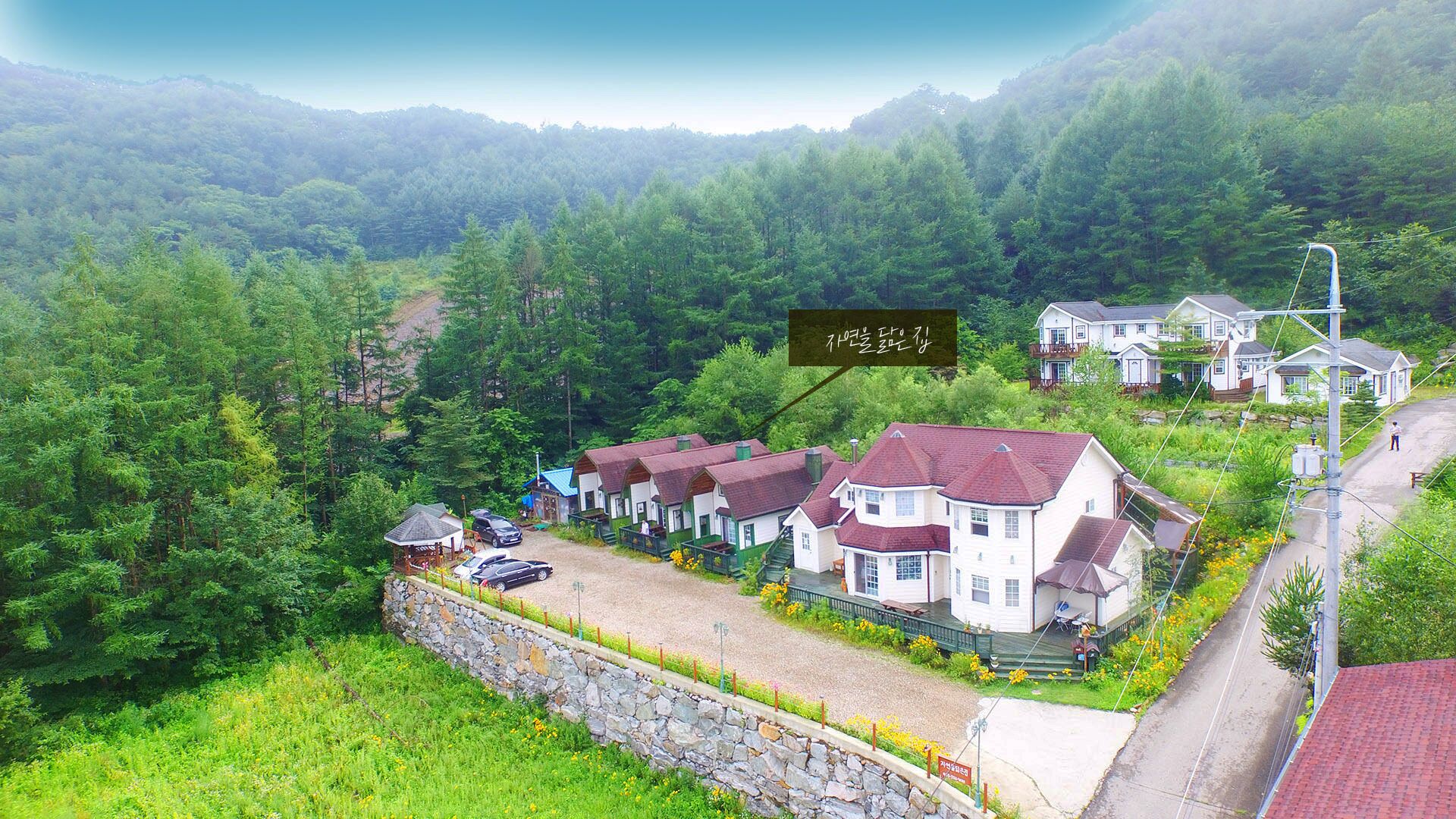 A row of traditional houses with red roofs, surrounded by lush greenery and a stone wall.
