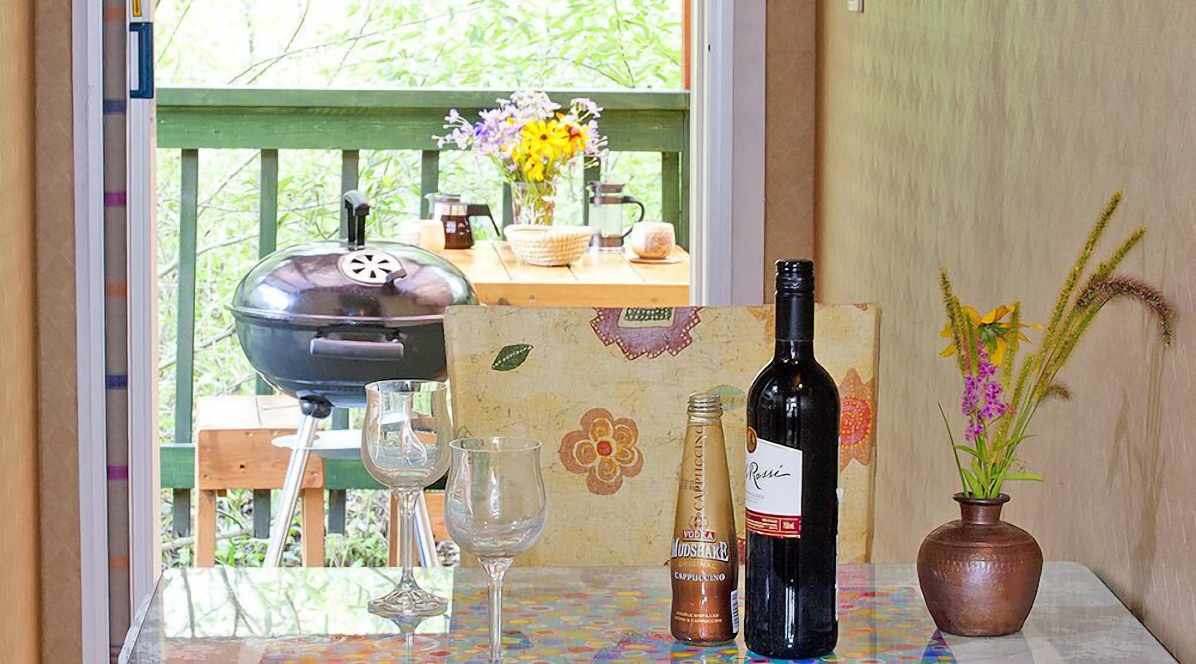 A table with a bottle of wine, a glass, a mug, and a vase with flowers.