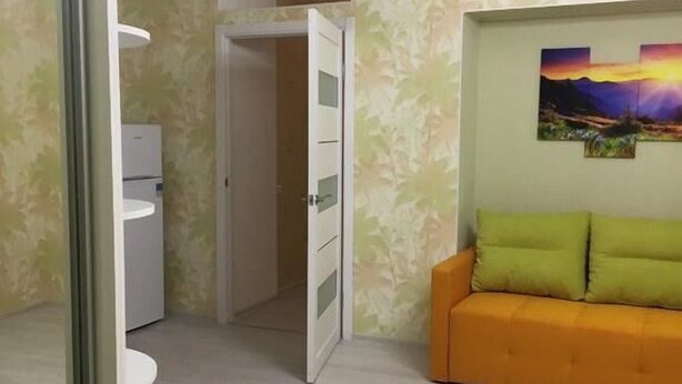 Huoneessa on puulattia, valkoinen vaatekaappi, vihreä sohva koristetyynyineen ja seinällä oleva taulu.