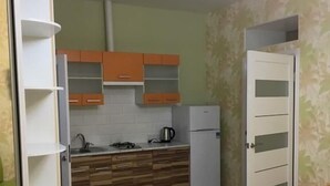 Kompakti keittiö, jossa on puiset kaapit, valkoinen jääkaappi ja sisäänrakennettu uuni.