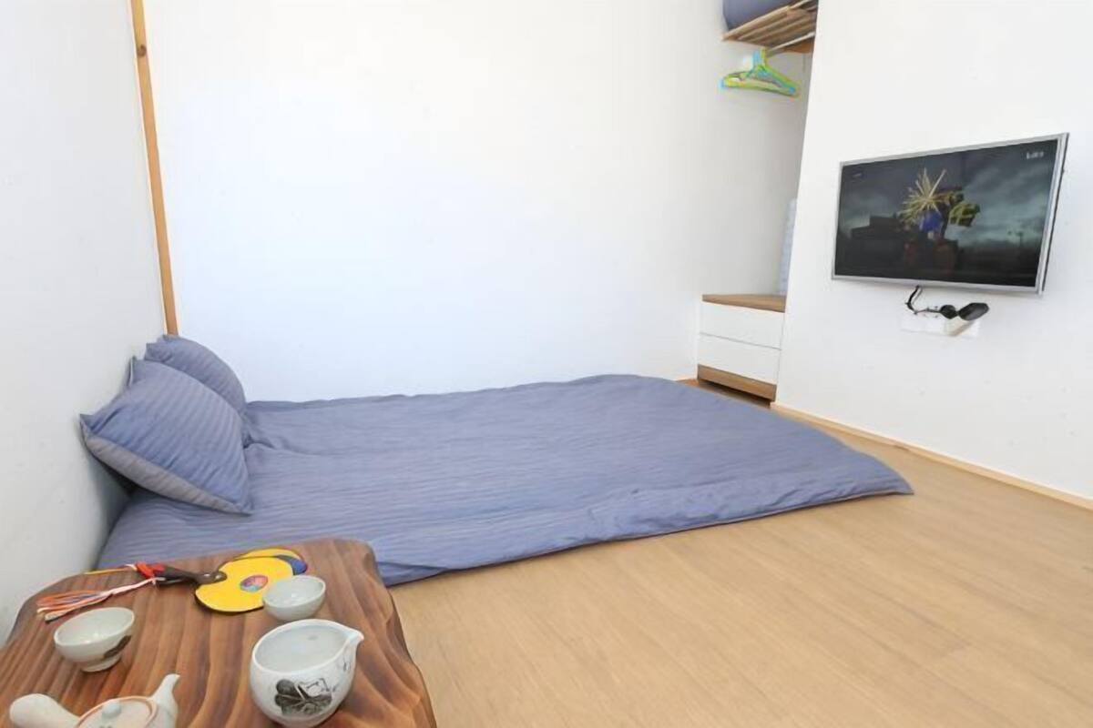 A room with a bed, a small table with a teapot, cups, and a mat.