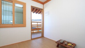Une pièce dotée d’un plancher en bois, d’une porte coulissante donnant sur un balcon, et d’une petite table en bois sur laquelle se trouvent des tasses et une assiette.