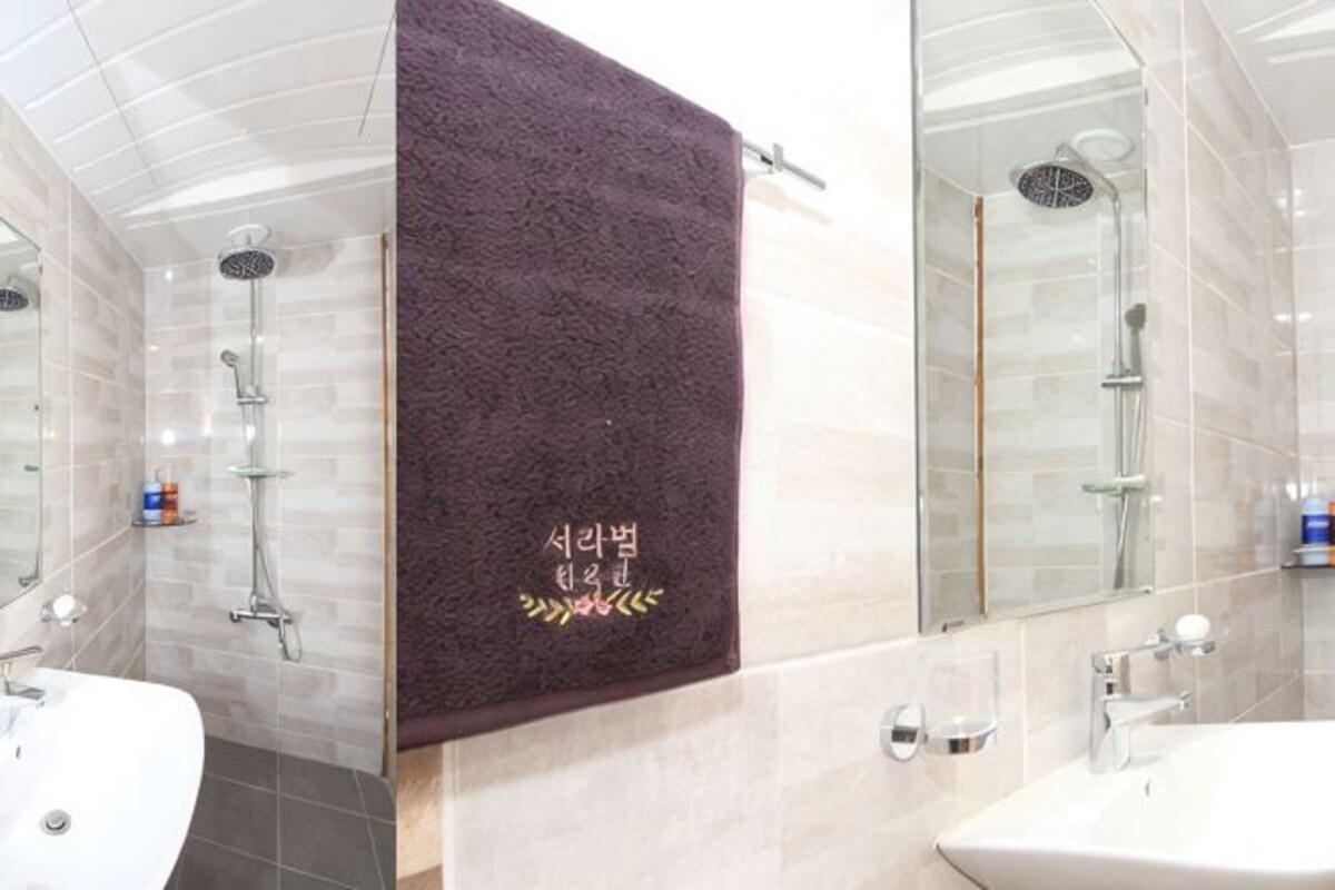 A modern bathroom with a glass shower enclosure, a white sink, and a marble-tiled wall.