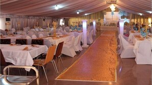 A banquet hall with multiple round tables covered with white tablecloths and chairs, a central aisle, and a decorative carpet. - Somitel Hotel And Resort (Port Harcourt)