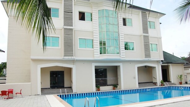 A two-story building with a swimming pool, red chairs, and potted plants. - Somitel Hotel And Resort (Port Harcourt)