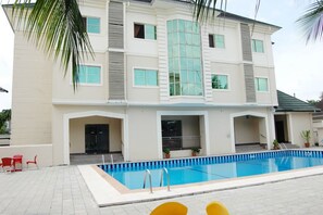 A two-story building with a swimming pool, red chairs, and potted plants. - Somitel Hotel And Resort (Port Harcourt)