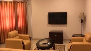A living room with a sofa set, a flat-screen TV, a lamp, and an air conditioning unit. - Somitel Hotel And Resort (Port Harcourt)