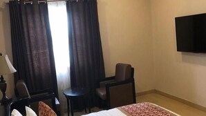 A hotel room with a bed, two chairs, a desk, an air conditioning unit, and a TV on the wall. - Somitel Hotel And Resort (Port Harcourt)