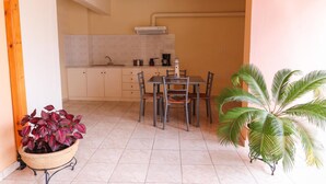 A compact kitchen with a dining area, featuring a tiled floor, a dining table with chairs, and a potted plant.
