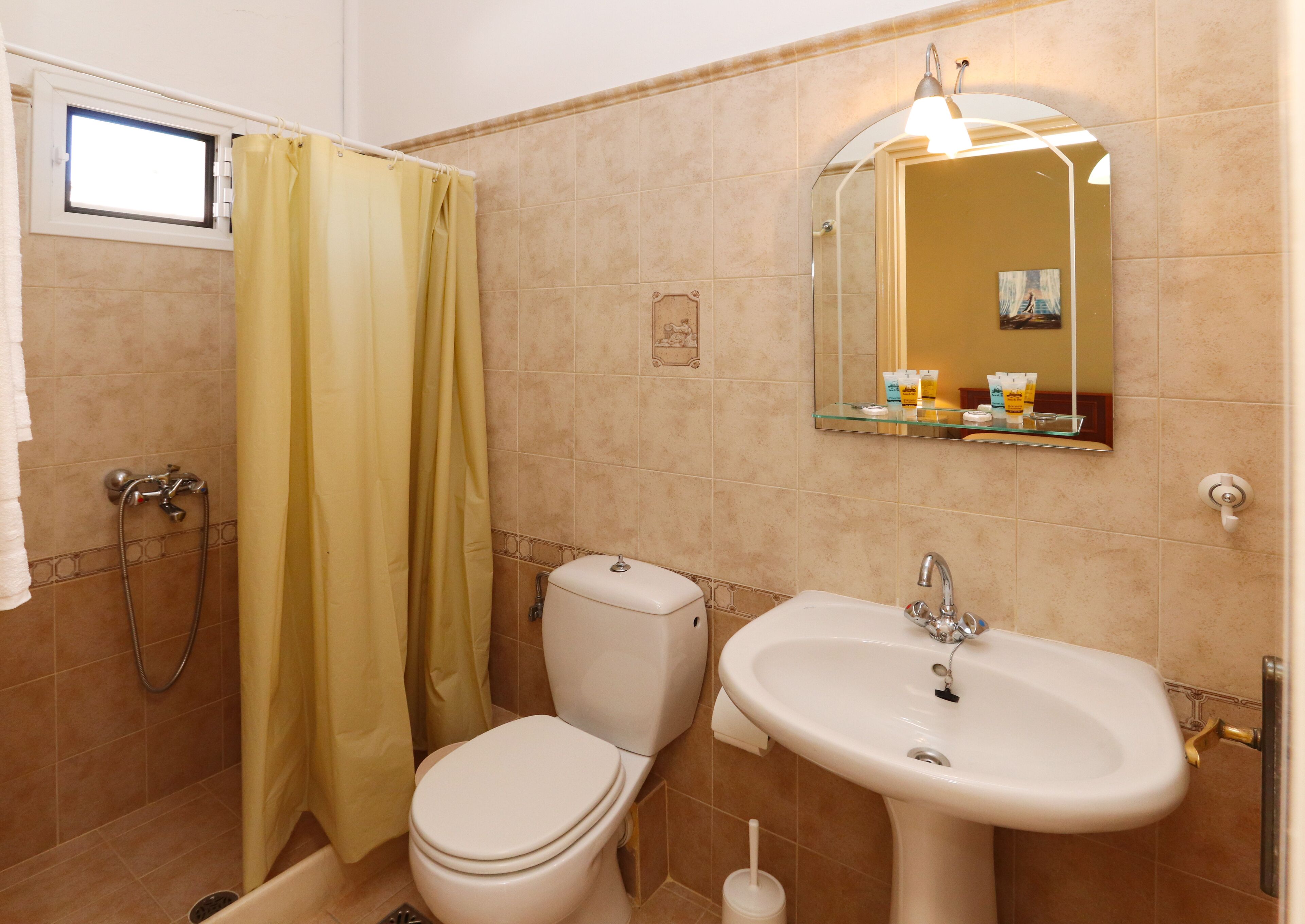 A bathroom with a toilet, sink, shower, and a mirror.