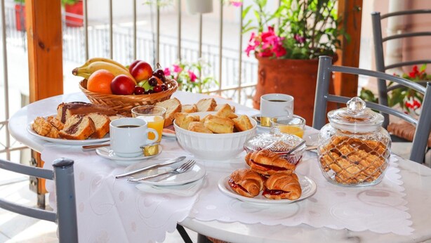 A breakfast table with croissants, pastries, a fruit bowl, and a coffee cup.