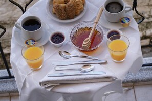 Una bandeja de desayuno con café, jugo, miel y croissants sobre una mesa.