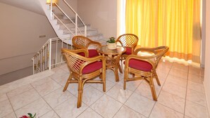 A room with a dining table, four wicker chairs with red cushions, a potted plant, and a staircase with a railing.
