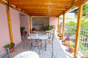 Un patio techado con mesas y sillas, plantas en macetas y vistas a una cocina y jardín.