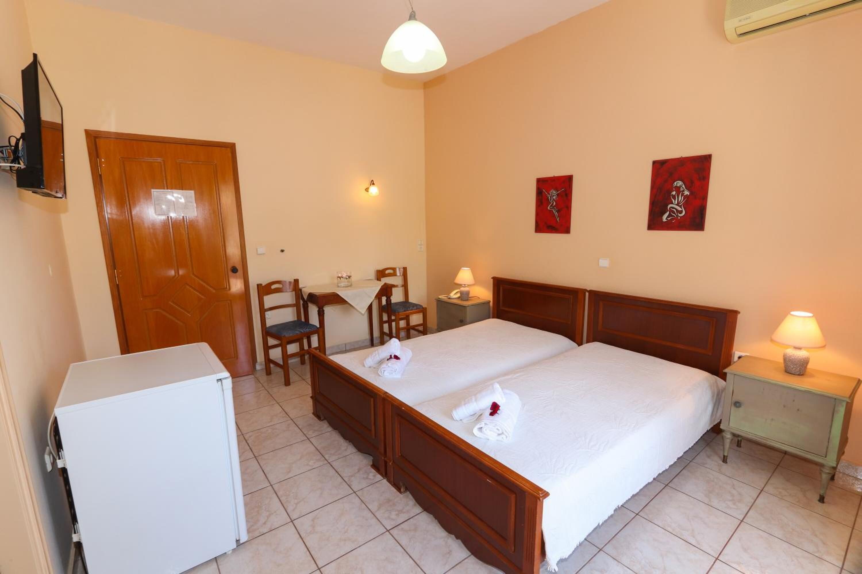 A hotel room with a double bed, a desk with a chair, a small refrigerator, and two wall-mounted lamps.