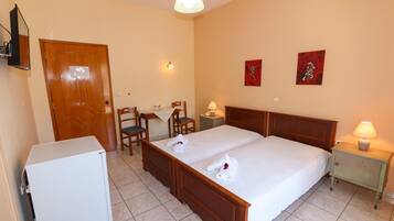 A hotel room with a double bed, a desk with a chair, a small refrigerator, and two wall-mounted lamps.