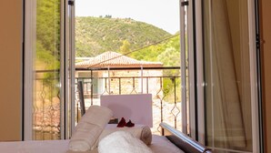A hotel room with a bed, a view of a hillside, and a balcony with a railing.
