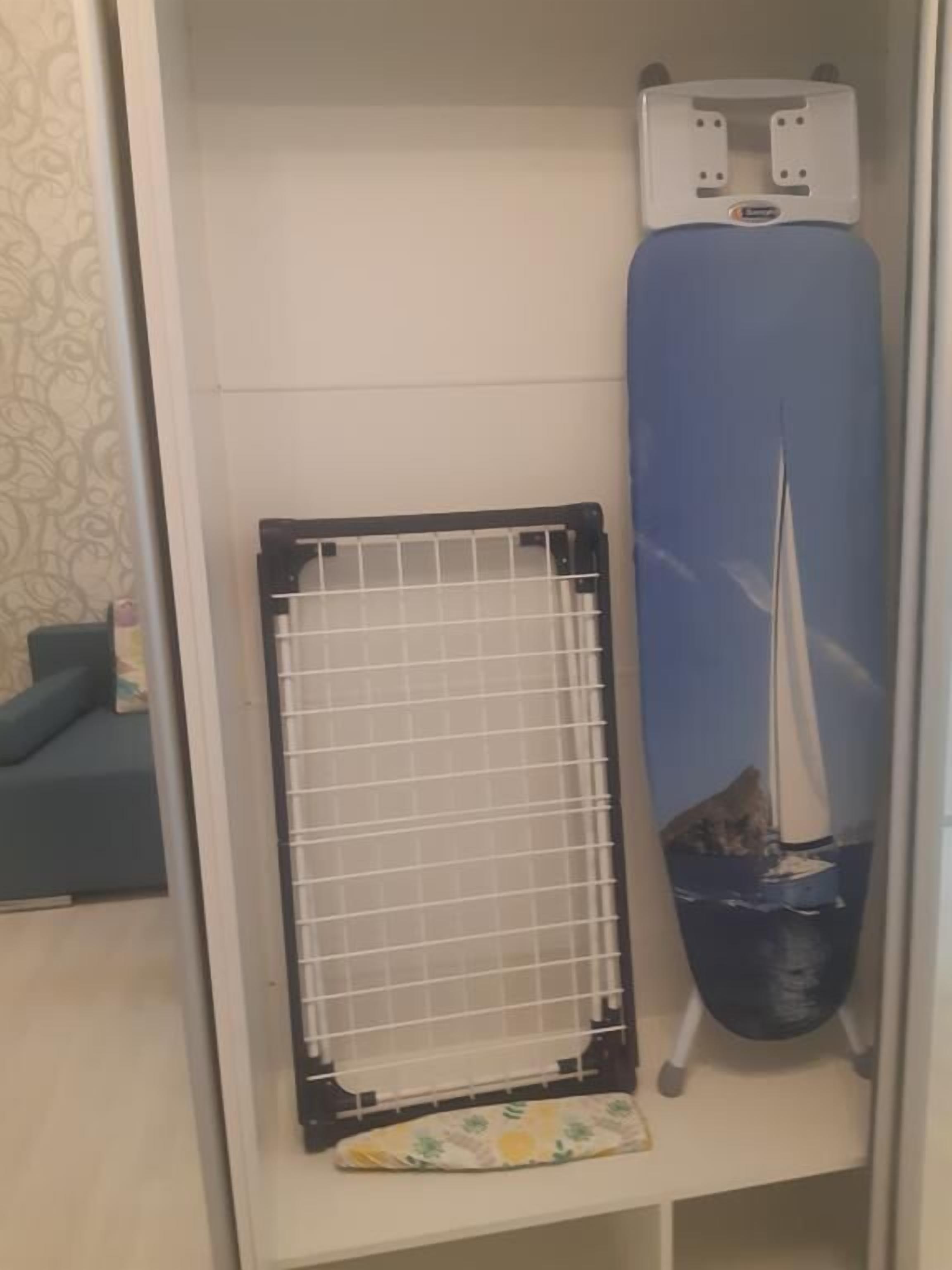 A closet with a hanging rack, a blue ironing board, and a white ironing board cover.