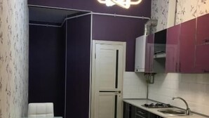 A compact kitchen with a dining area, featuring a modern pendant light, a refrigerator, and built-in cabinets.