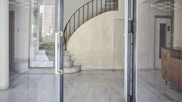 A modern interior with a curved staircase, a glass door entrance, and a marble floor.