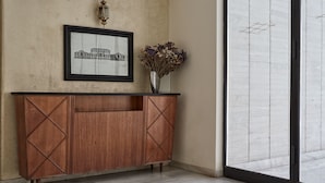 A reception area with a wooden console, a framed cityscape artwork, and a vase with dried flowers.