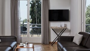 A modern living room with a leather sofa, a coffee table with a cup and glass, a TV mounted on the wall, and a balcony with a table and chairs.