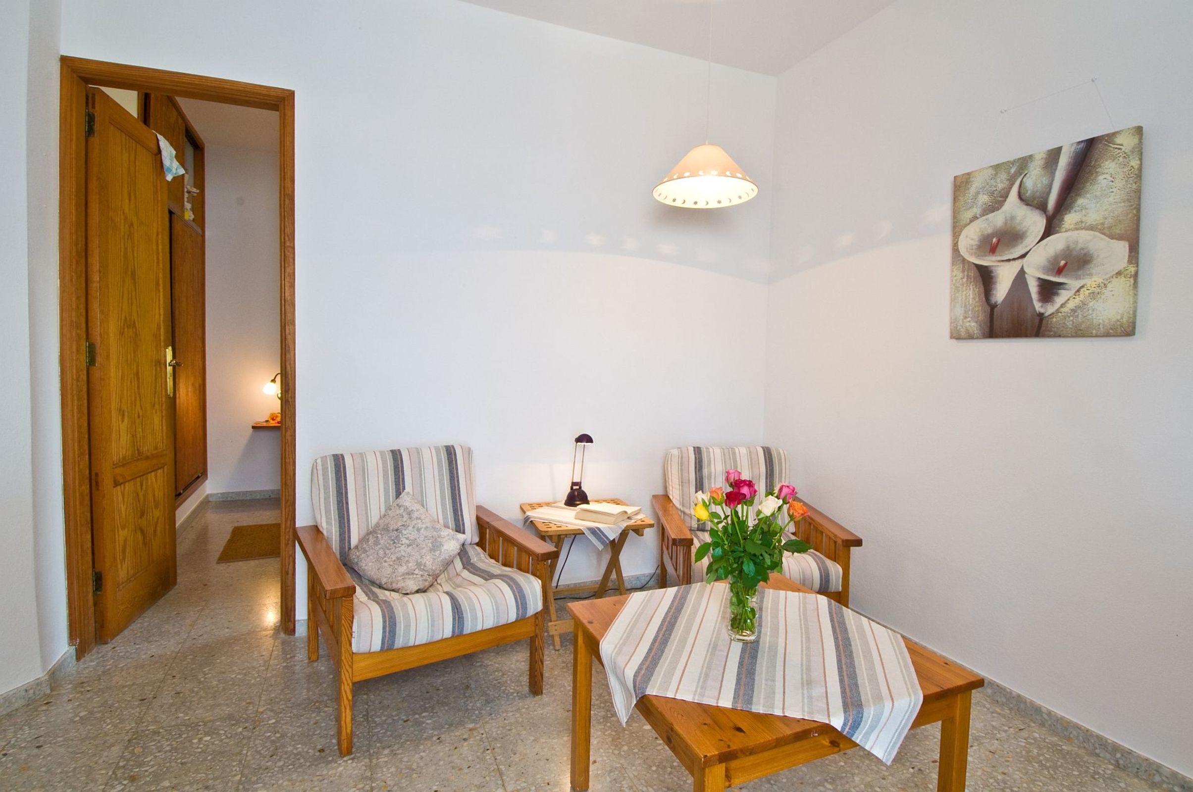 Een gezellige kamer met een houten deur, twee gestreepte fauteuils, een kleine tafel met een bloevas en een wandlamp.