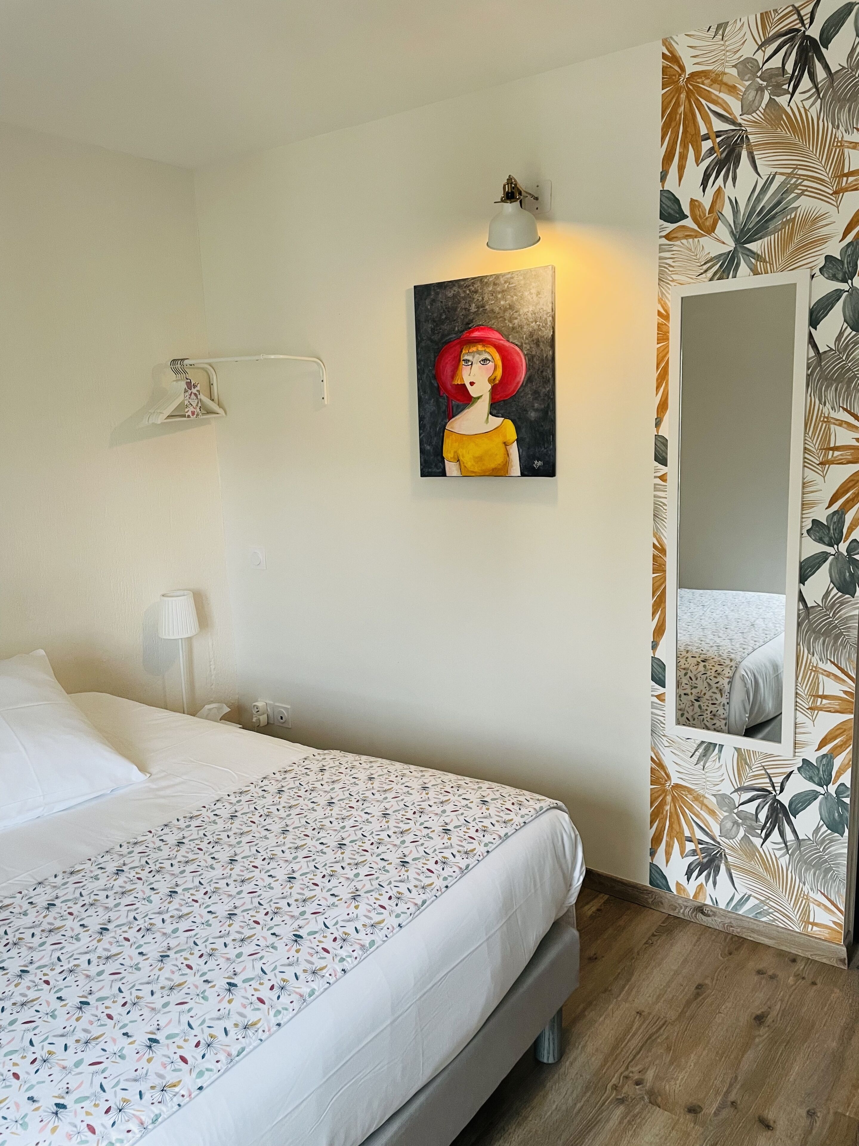 A bedroom with a bed, a painting, a lamp, and a mirror.