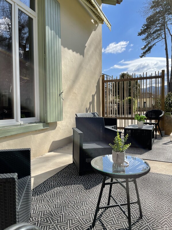 An outdoor patio with wicker furniture, a glass table, and a patterned floor.