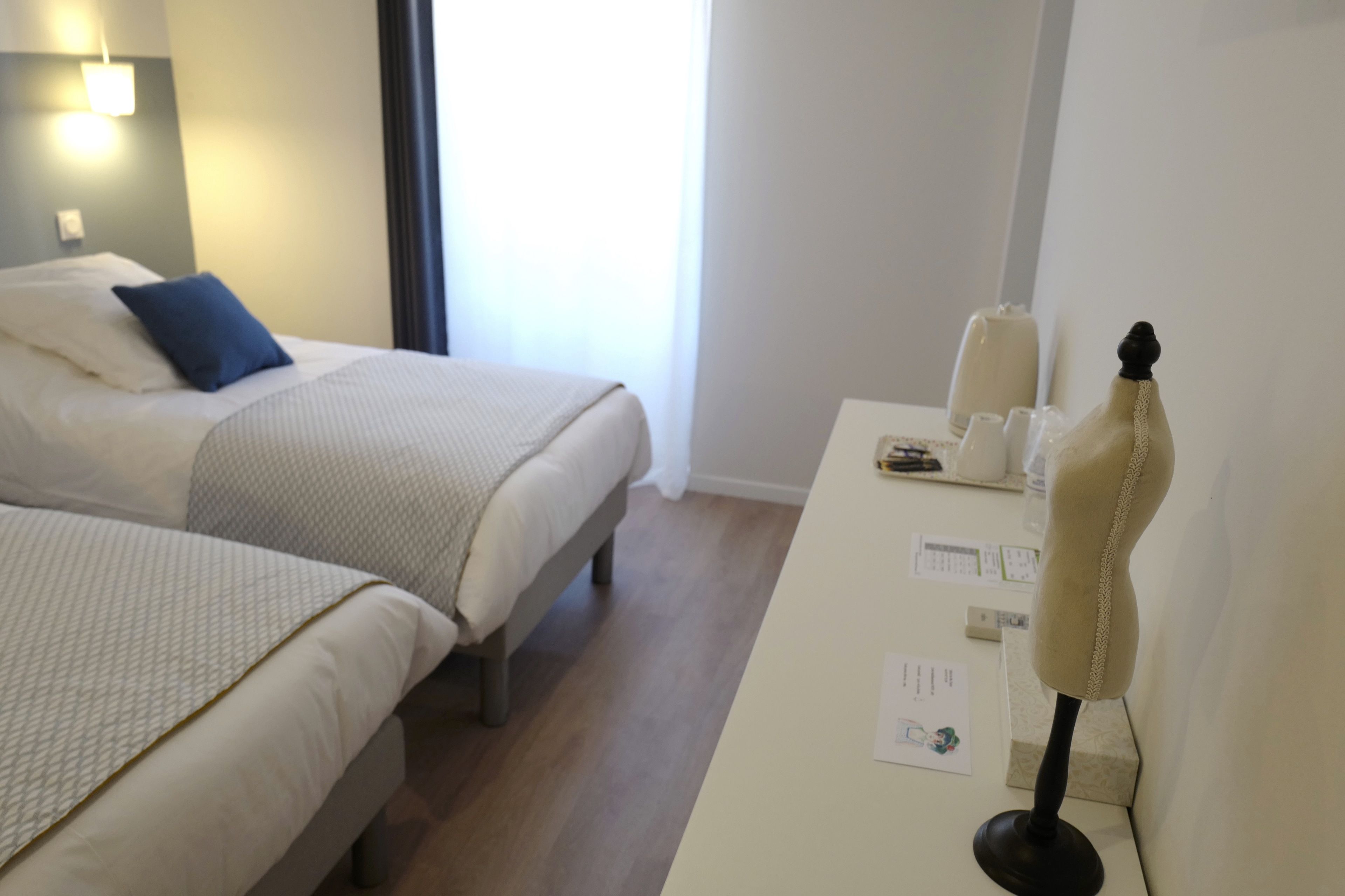 Une chambre d’hôtel avec deux lits, un bureau avec un mannequin et une fenêtre avec des rideaux.