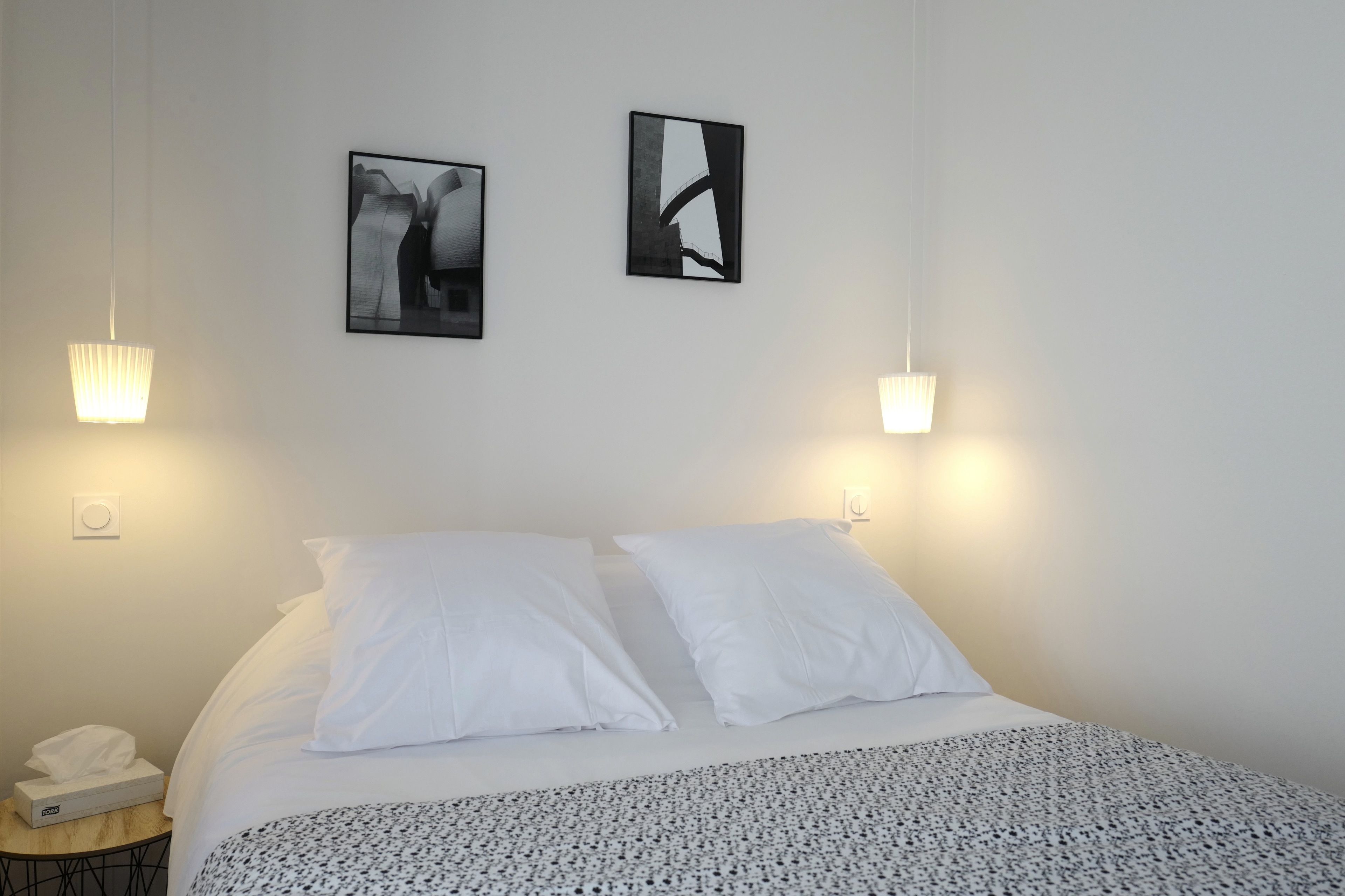 A hotel room with a neatly made bed, two wall-mounted lamps, and two framed artworks.